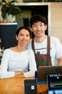 Portrait of two smiling coffee shop owners standing behind counter. Ideal for business and small enterprise themes.